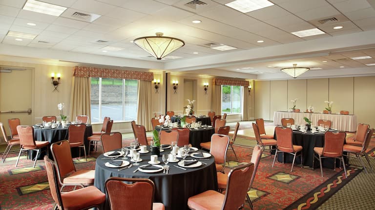Round Dining Tables With Place Settings and Flowers on Black Linens in Ballroom Set Up for Business Reception
