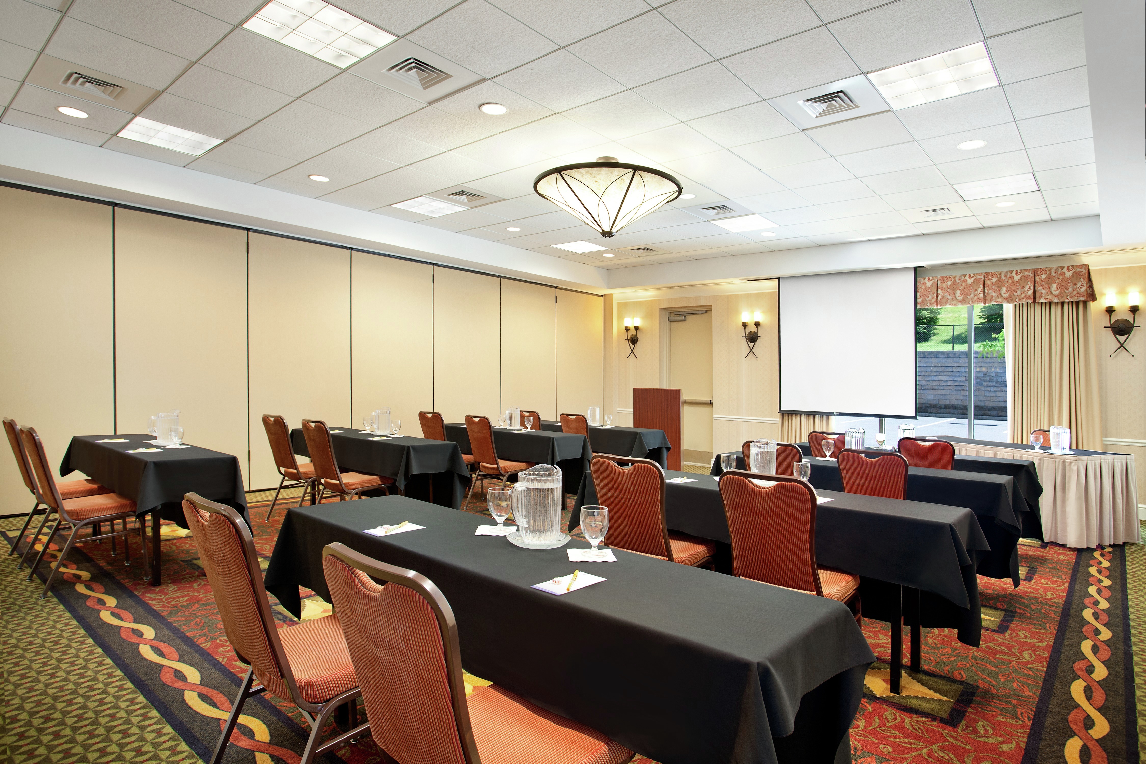 Classroom Setup in Meeting Room With Tables and Chairs Facing Presentation Screen and Window With Open Drapes