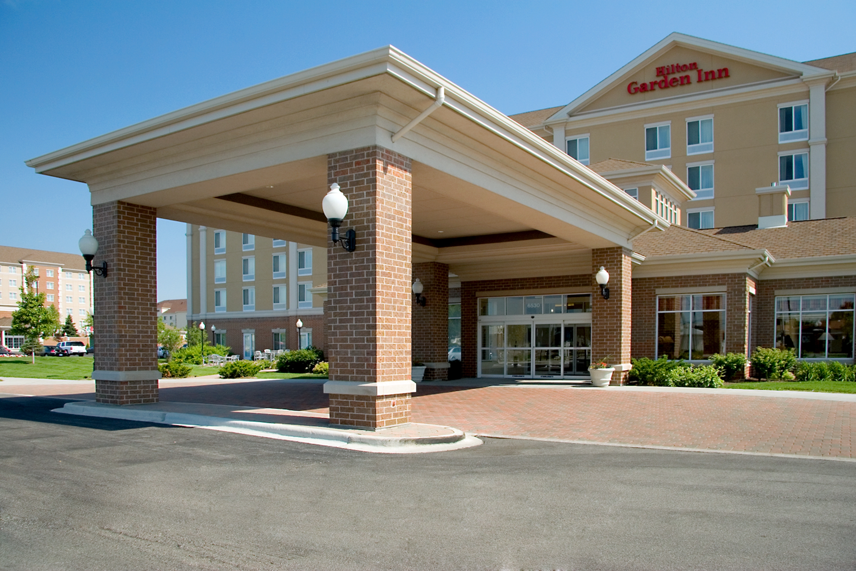 Daytime View of Hotel Exterior With Signage, Entrance, Landscaping, and Porte Cochère