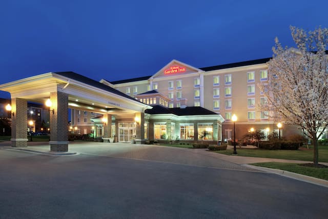 Illuminated Hotel Exterior With Signage, Entrance, Porte Cochère, Flagpoles, and Landscaping at Night