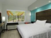 One King Bed Guest Room with Bright Blue Accent Wall behind Large Wooden Headboard 