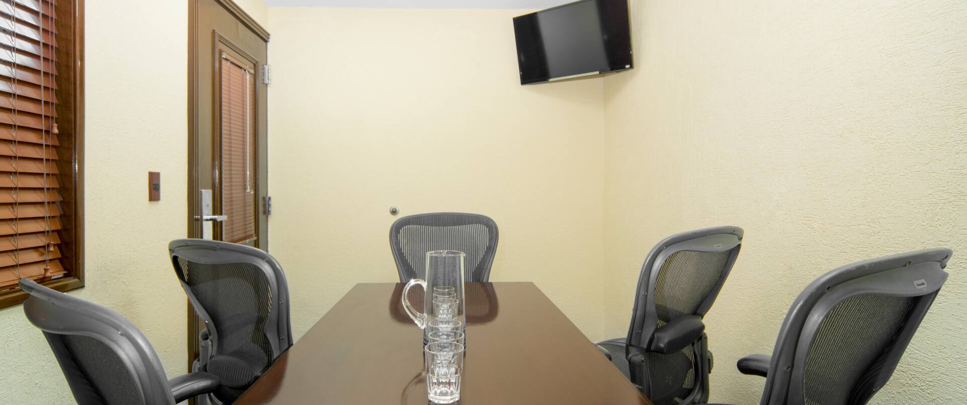 Sala de juntas con mesa de reuniones, sillas de oficina y televisor de alta definición montado en la pared