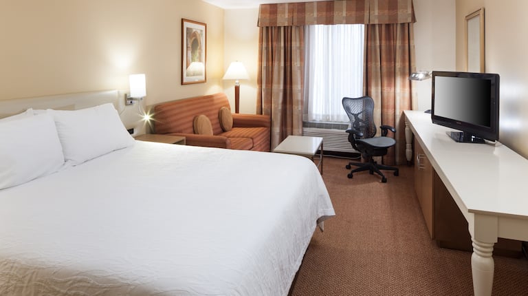 标准客房内设有特大床、照明灯、床头柜、墙面装饰画、沙发床、照明落地灯、长窗帘窗户、工作桌和电视