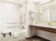 Spacious accessible bathroom featuring tub with seat and grab bars for guest safety.