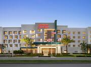 Welcoming hotel exterior featuring glowing guest room windows, large palm trees, and dusk sky.