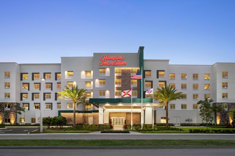 Welcoming hotel exterior featuring glowing guest room windows, large palm trees, and dusk sky.