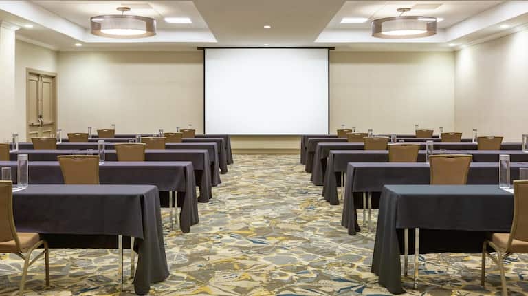 Spacious ballroom  featuring classroom setup with tables, chairs, and projector screen at front of room.
