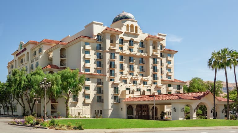 Embassy Suites hotel exterior featuring lush grass, towering palm trees, and view of the mountains.