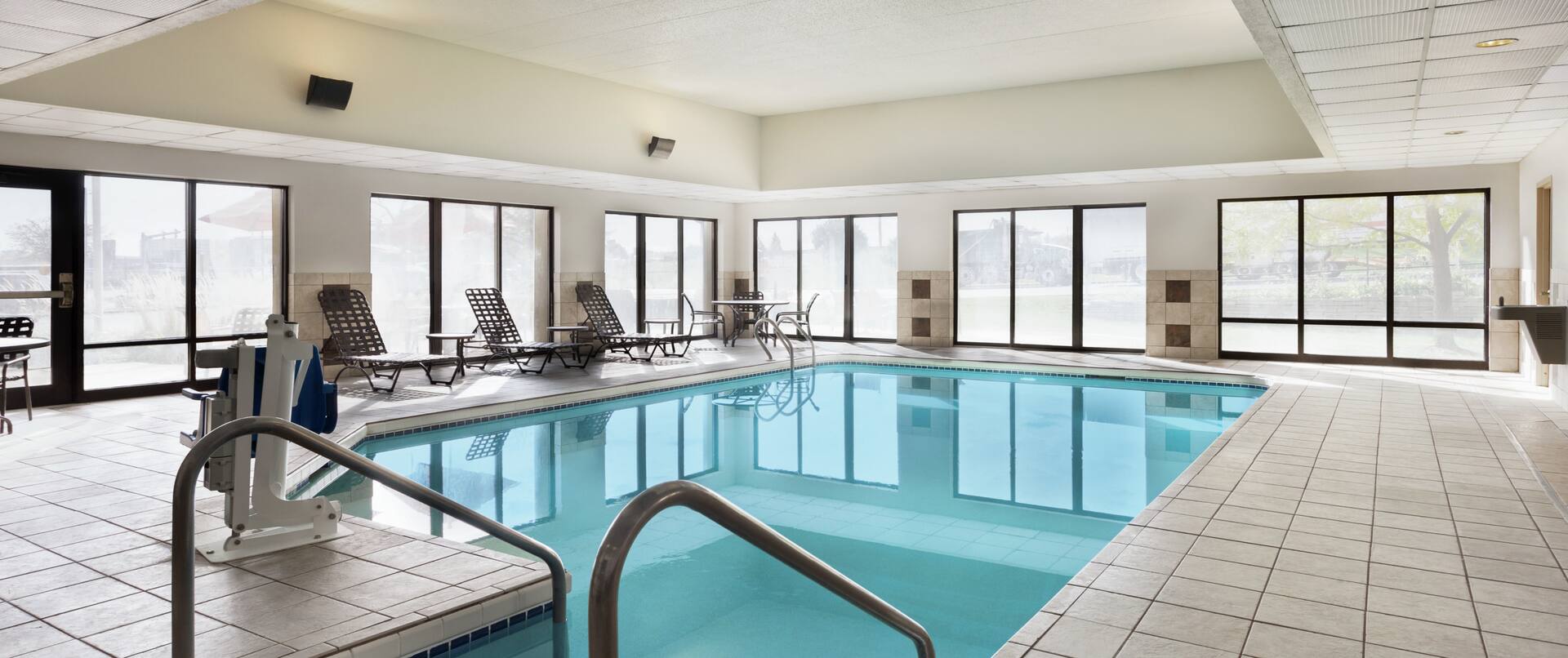Spacious indoor pool featuring accessible chair lift, ample seating, and large floor to ceiling windows.
