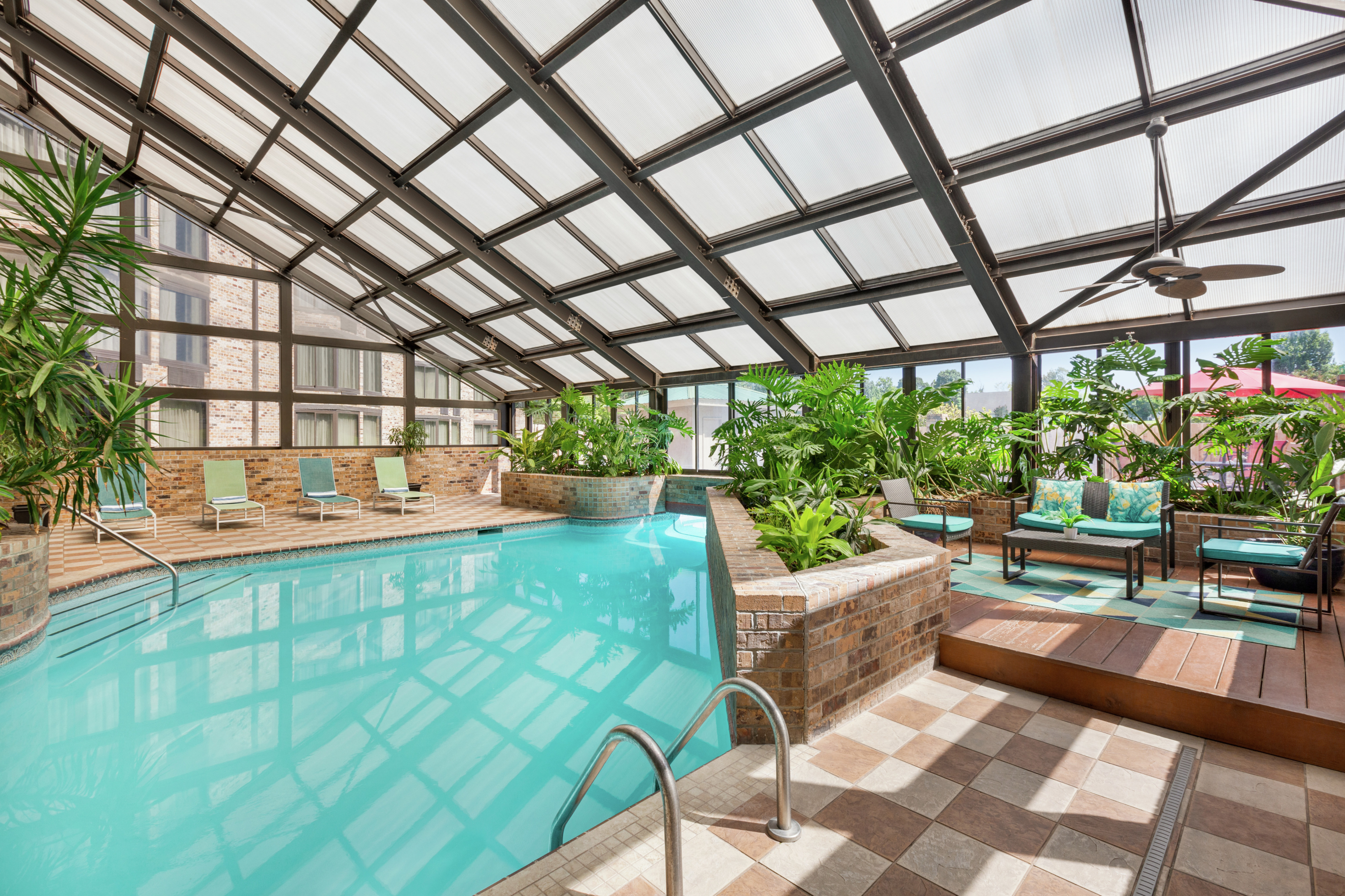 Spacious on-site indoor pool featuring ample light, lush greenery, and comfortable seating.