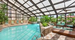 Spacious on-site indoor pool featuring ample light, lush greenery, and comfortable seating.