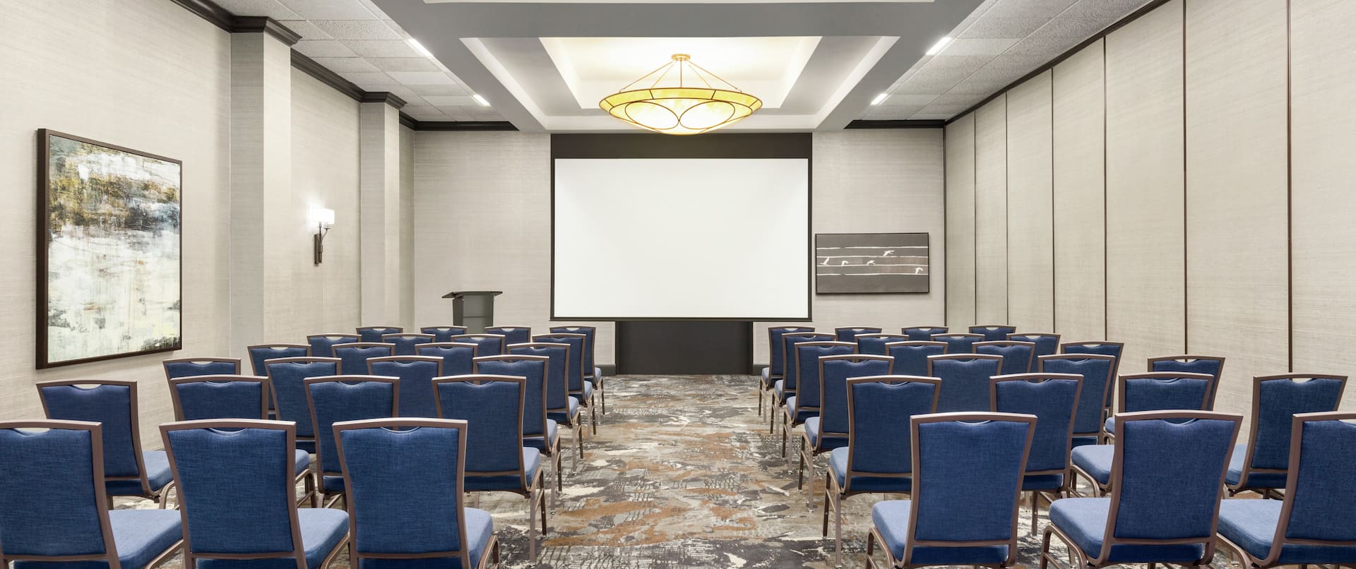 Spacious on-site meeting room featuring theater style setup and projector screen at front of room.