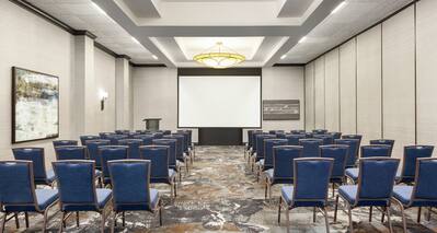Spacious on-site meeting room featuring theater style setup and projector screen at front of room.