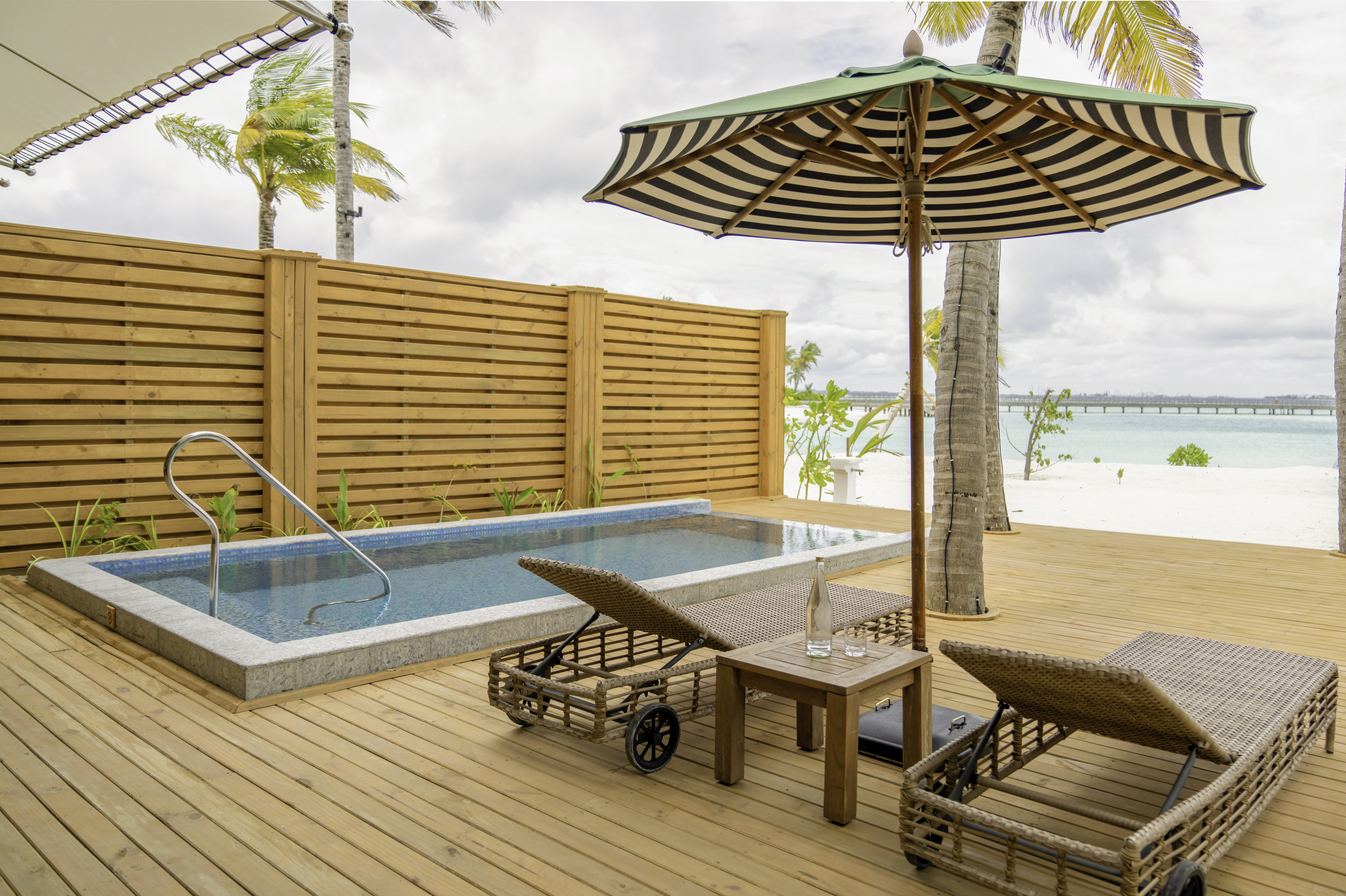 Outdoor Pool Area with Lounge Chairs under an Umbrella and View of the Beach