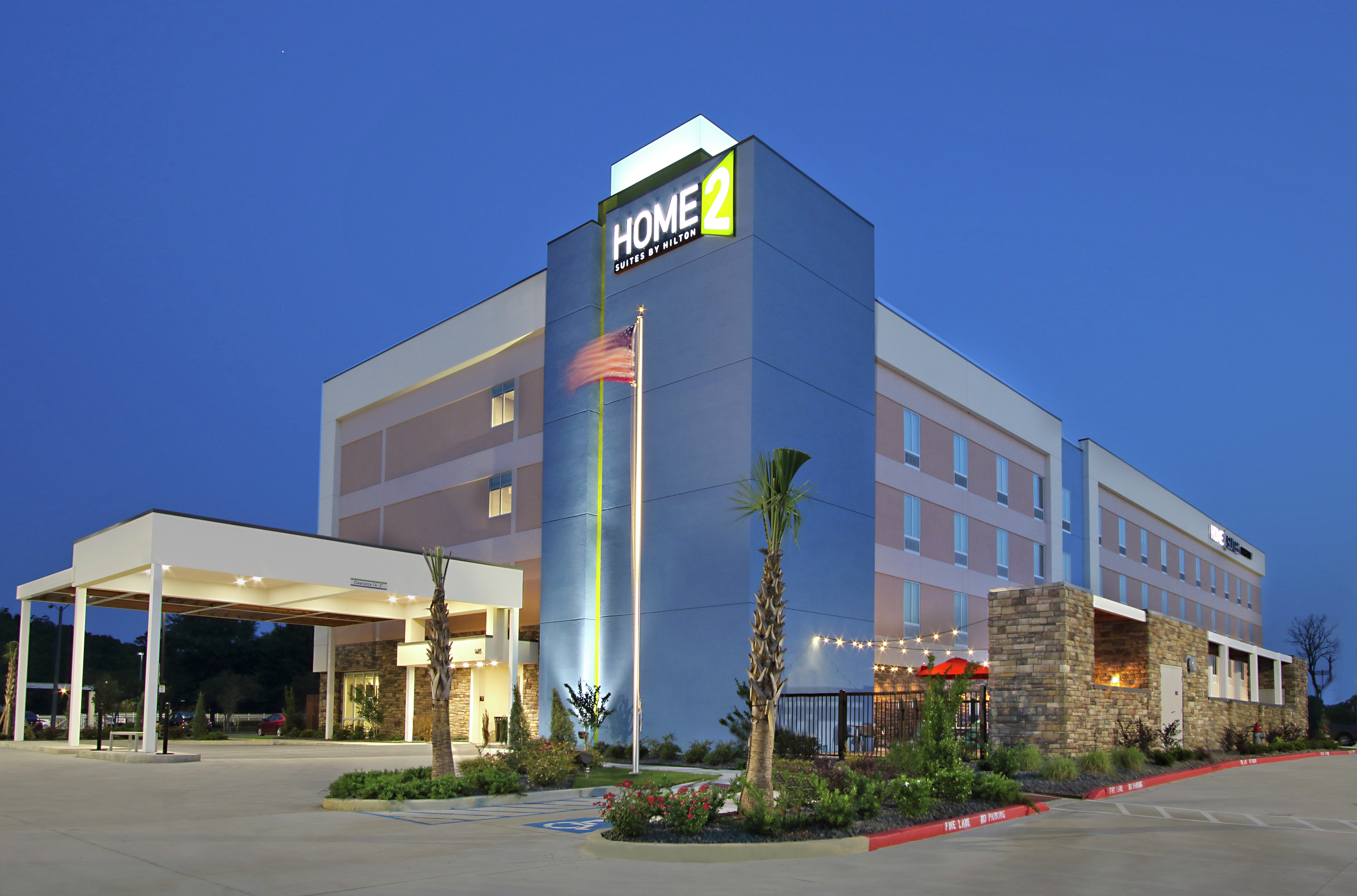 Illuminated Hotel Exterior With Signage, Porte Cochère, Flagpole, and Landscaping at Dusk