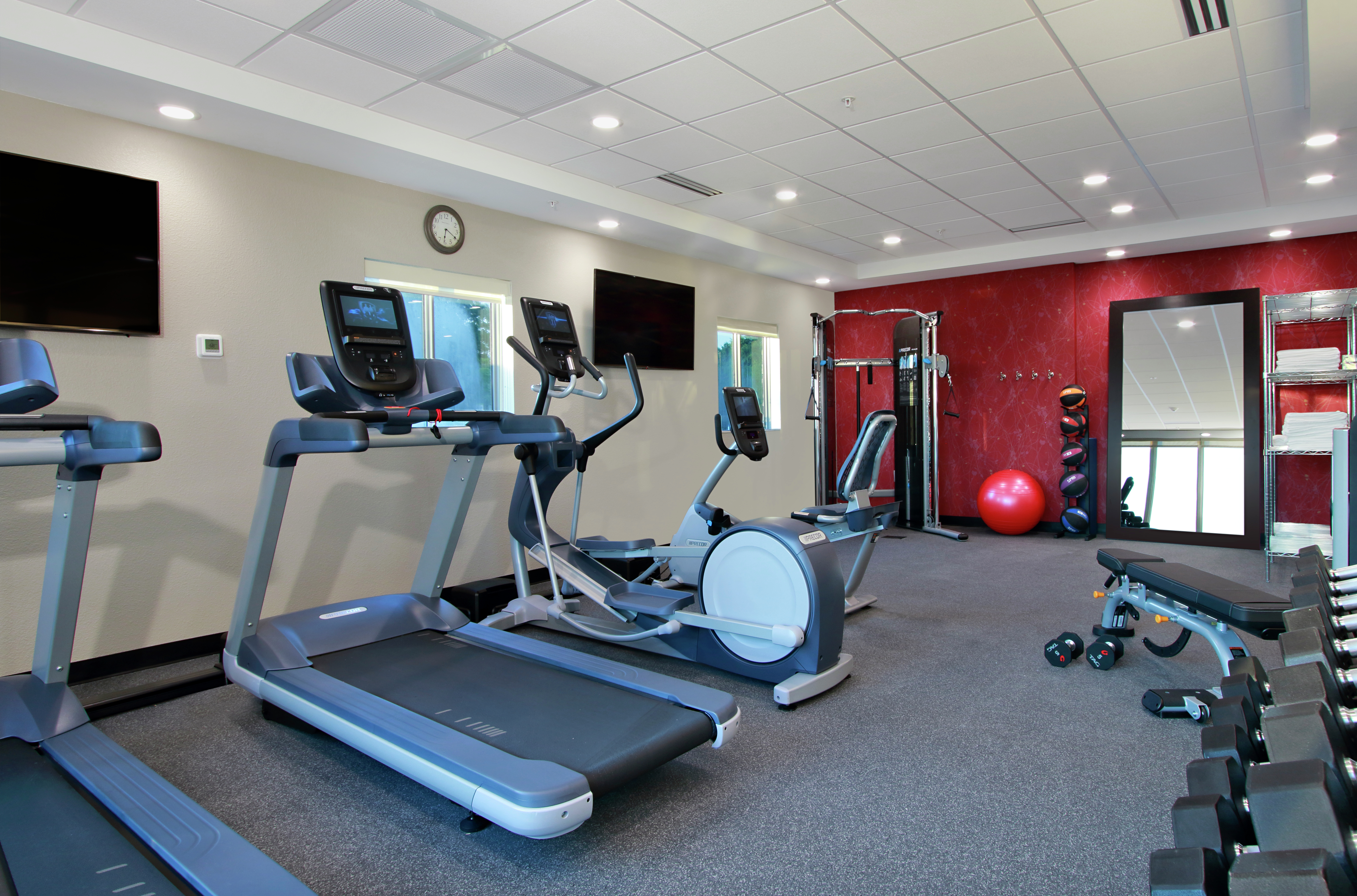 Fitness Center With TVs,  Cardio Equipment, Weight Machine, Red Stability Ball, Weight Balls, Large Mirror, Towel Station, Bench, and Free Weights