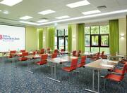 Classroom Setup in Meeting Room With Tables and Chairs Facing Large Presentation Screen and Windows With Long Green Drapes