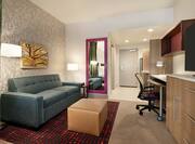 Bright studio suite featuring lounge area with TV, work desk, and fully equipped kitchen.