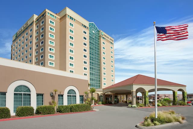 Embassy Suites hotel exterior featuring porte cochere, American flag on pole, and convention center.