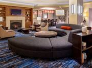 Lobby seating area with curved sofa, ottoman, soft chairs, coffee table, fireplace, and front desk