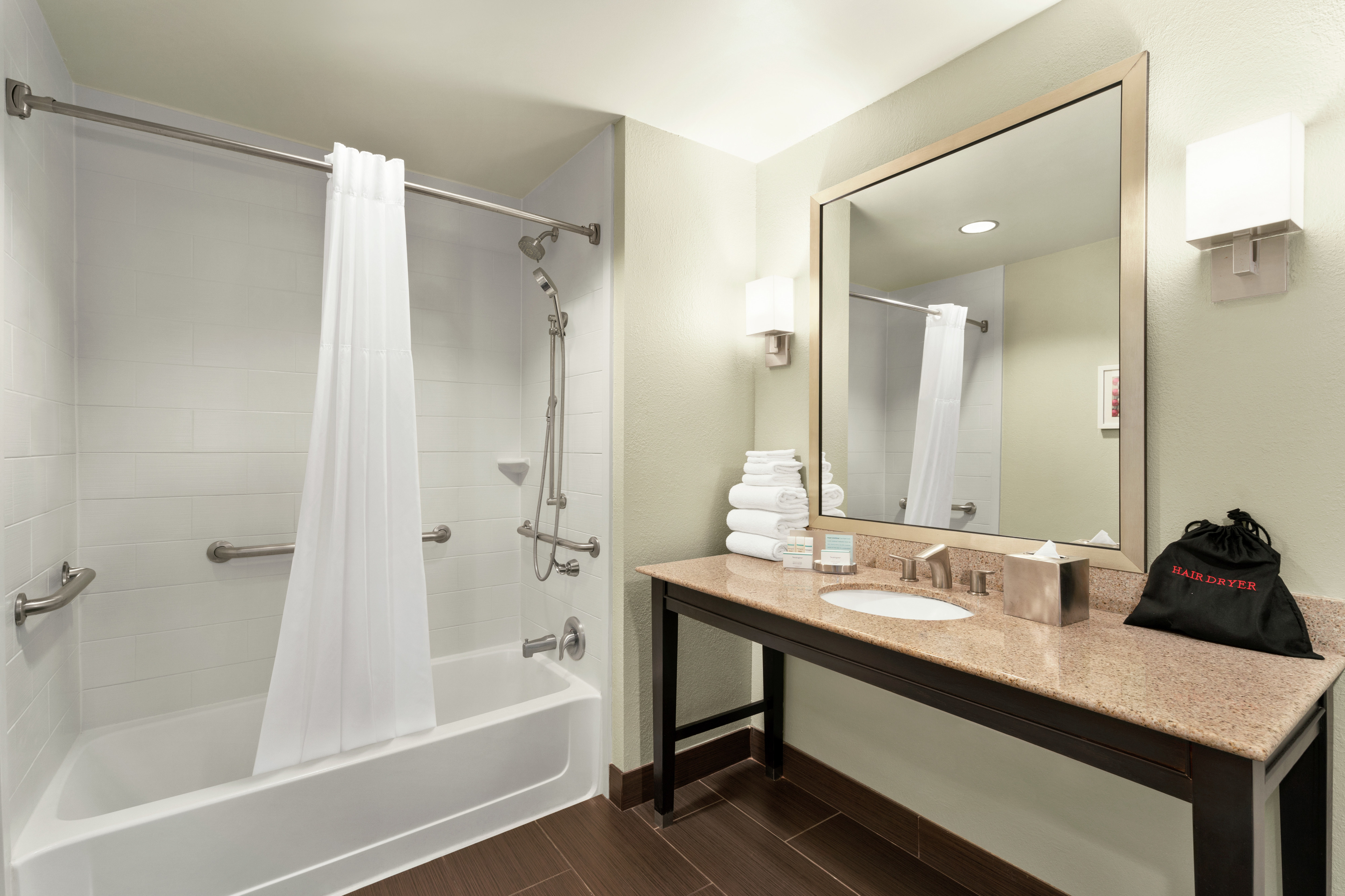 Spacious accessible bathroom featuring tub with grab bars, vanity, and mirror.