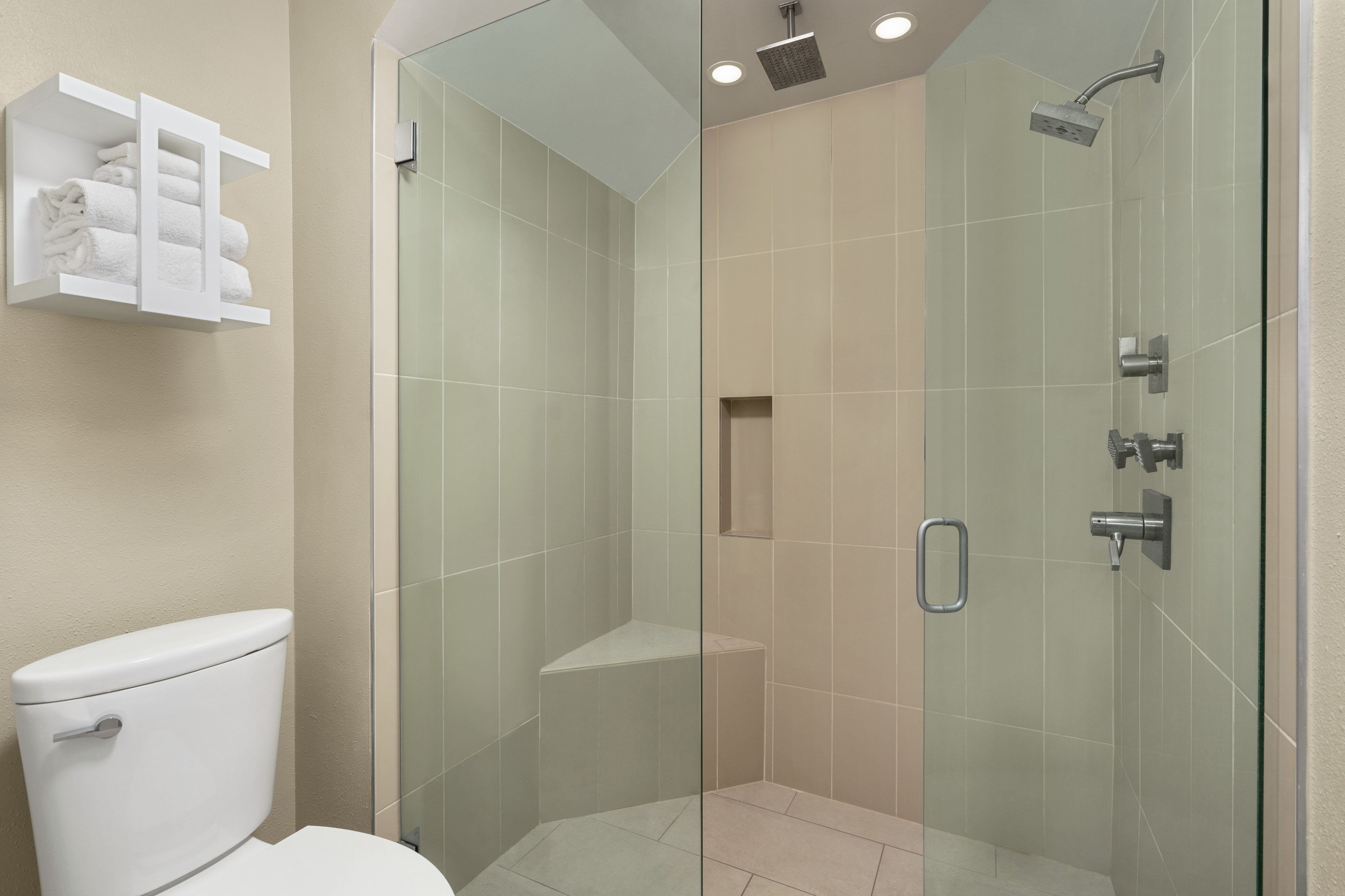 Spacious stand up shower with glass doors, dual shower head, and seating.