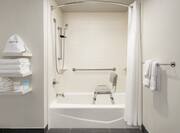 Spacious accessible bathroom featuring tub with shower seat and grab bars for guest safety.
