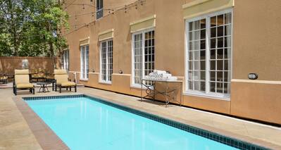 Spacious outdoor pool featuring privacy wall, ample lounge chairs, and lush greenery.