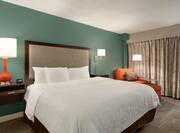 Spacious deluxe guest room featuring comfortable king bed, stylish design, and chaise lounge chair.