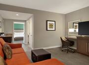 Spacious living area in suite featuring sofa, work desk, TV, wet bar, and view into private bedrom.