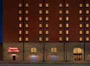 Historical hotel exterior featuring glowing guestroom windows and large Hampton Inn and Suites sign.