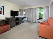 Sofa, TV, Work Desk, Window With Long Drapes, and Illuminated Floor Lamp in Suite