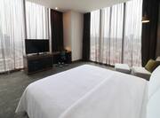 close up of king bed in accessible guest room, facing television with floor to ceiling windows around corner of the room