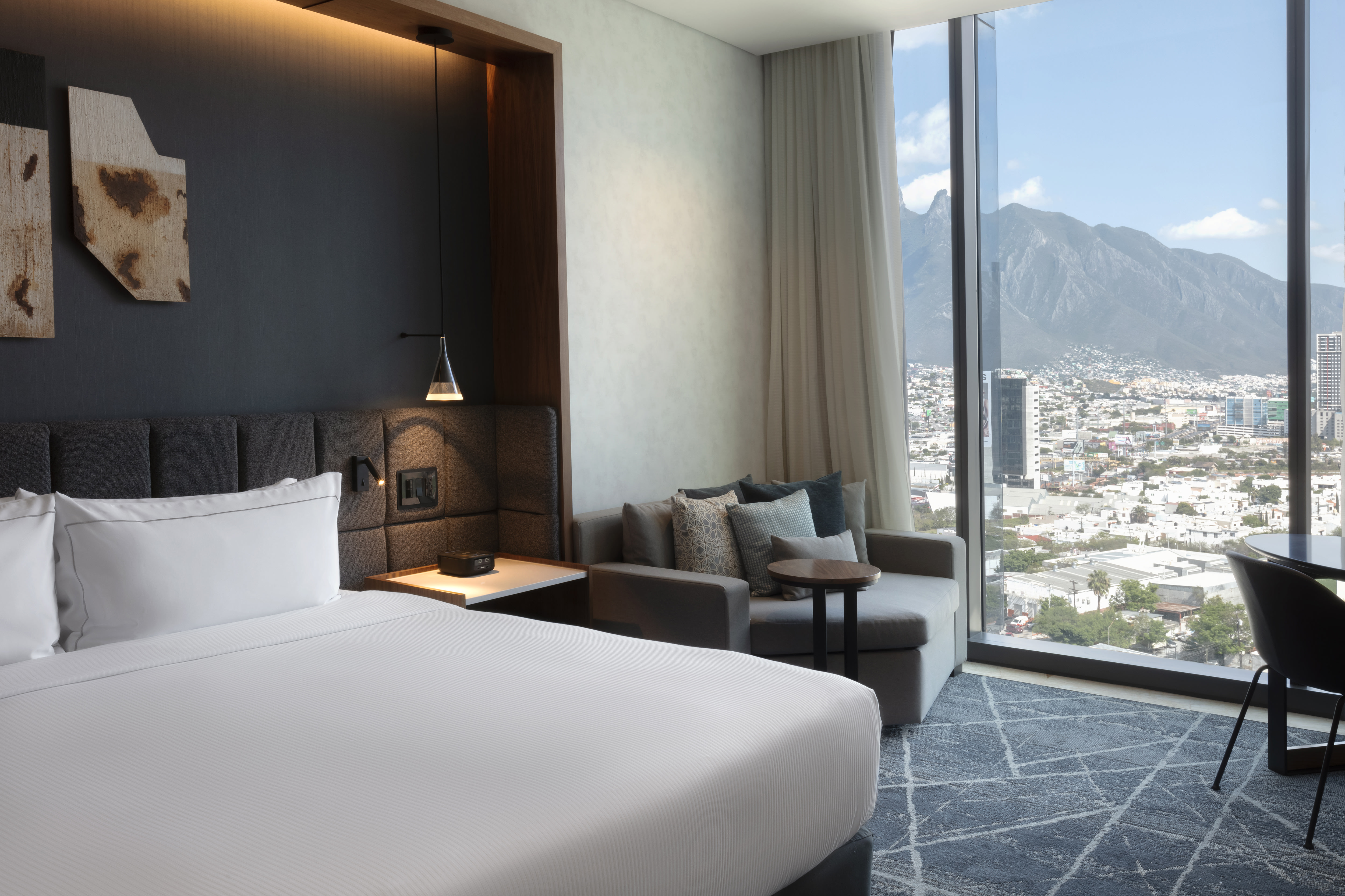 Guest room with king-sized bed, armchair and floor-to-ceiling windows with views of mountains and city