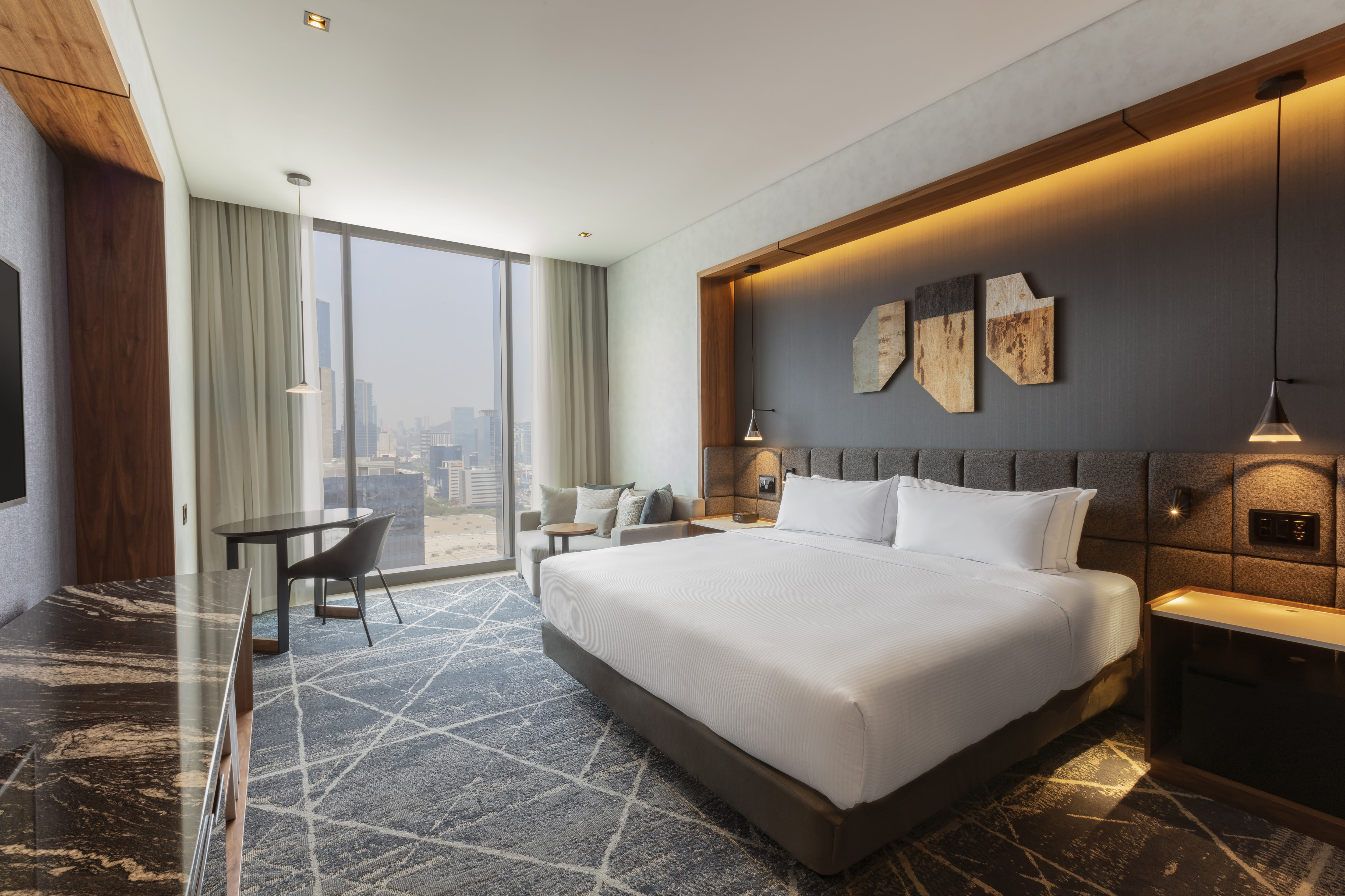 Guest room with king-sized bed, sofa and floor-to-ceiling windows with views of the city