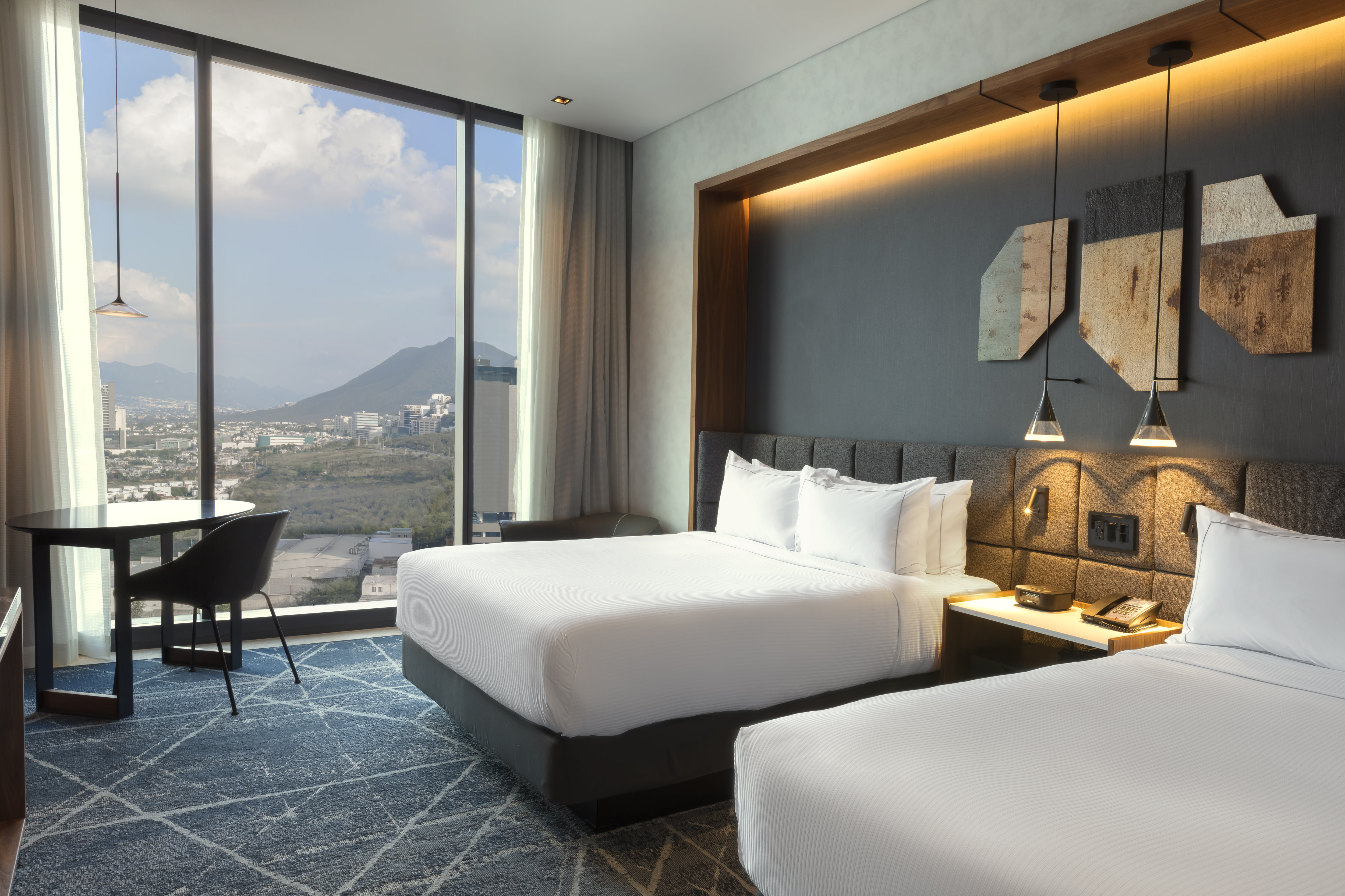 Guest room with two queen-sized beds and floor-to-ceiling windows with views of mountains and city