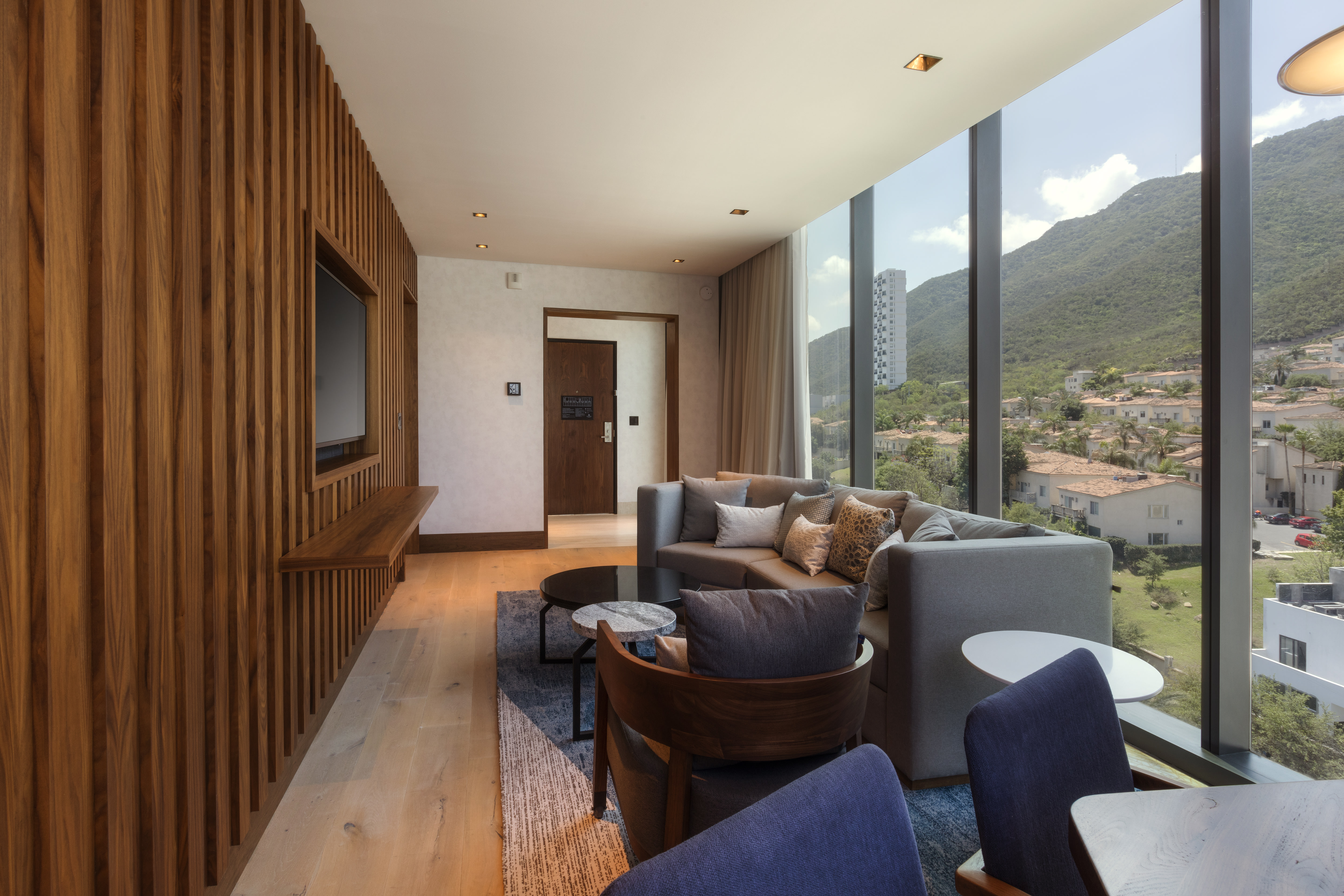 Suite living room with sofa, table and chairs, TV, and floor-to-ceiling windows with views of mountains and city