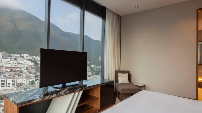 Guest room with king-sized, TV and floor-to-ceiling windows with views of mountains and city