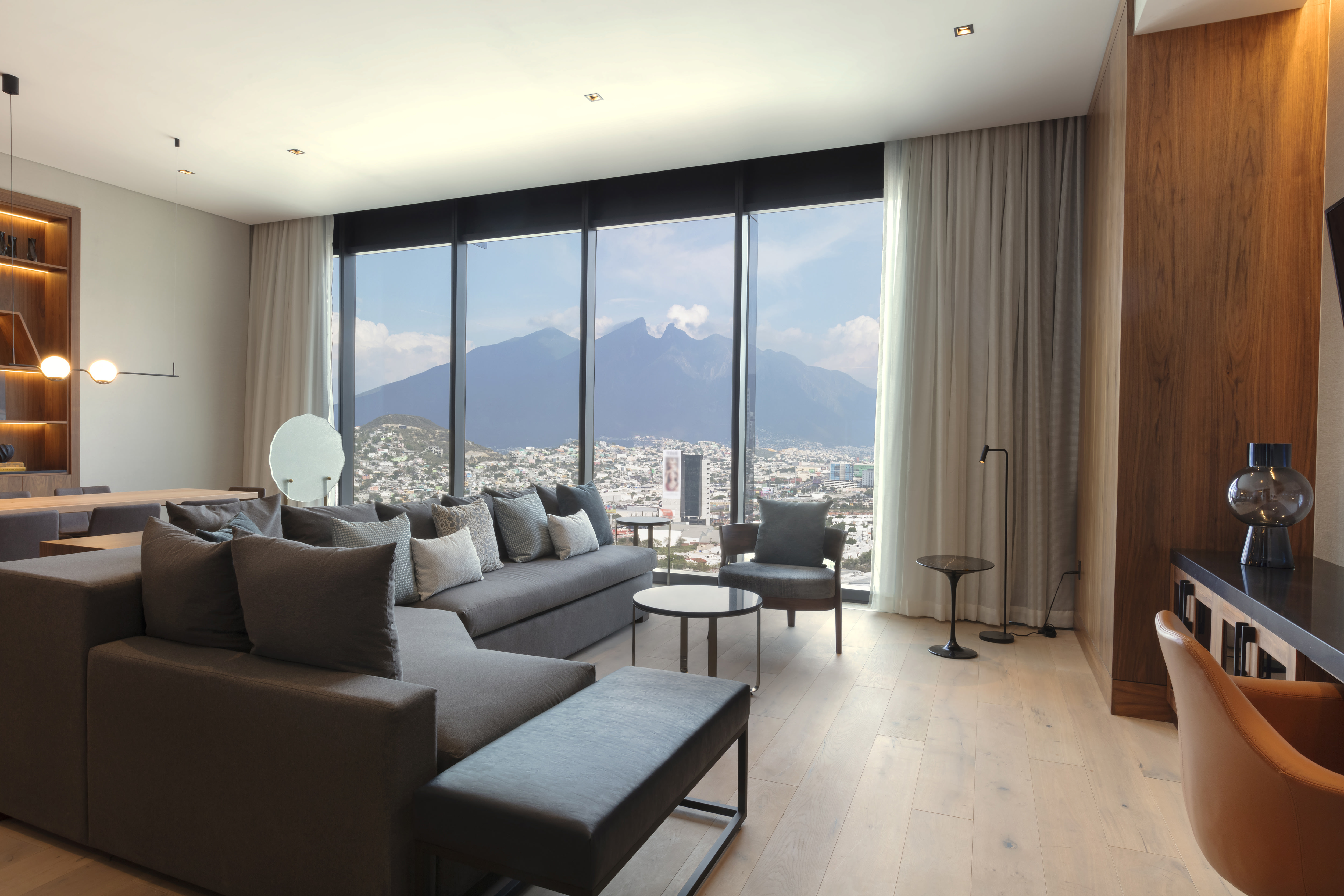 Suite living room with large sofa, dining table for 8 and floor-to-ceiling windows with views of mountains and city