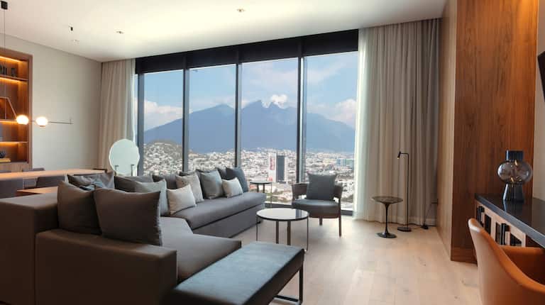 Sala de estar de la suite con sofá grande, mesa de comedor para 8 y ventanales con vista a las montañas y a la ciudad