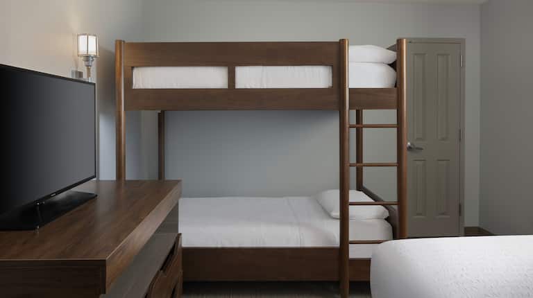 Bunkbeds in a hotel room with a twin bed and a TV on a cabinet.