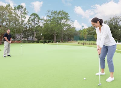 Woman Holding Putter on Putting green with Man Standing in Background