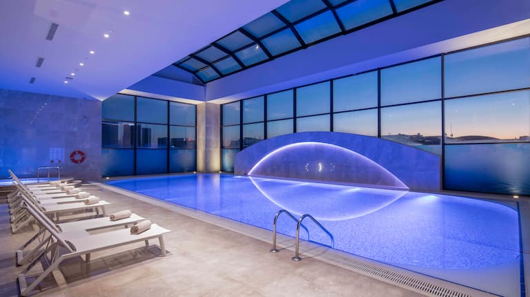  Lounge Seating by Indoor Pool With Large Windows, Blue Lighting, and Sunset View