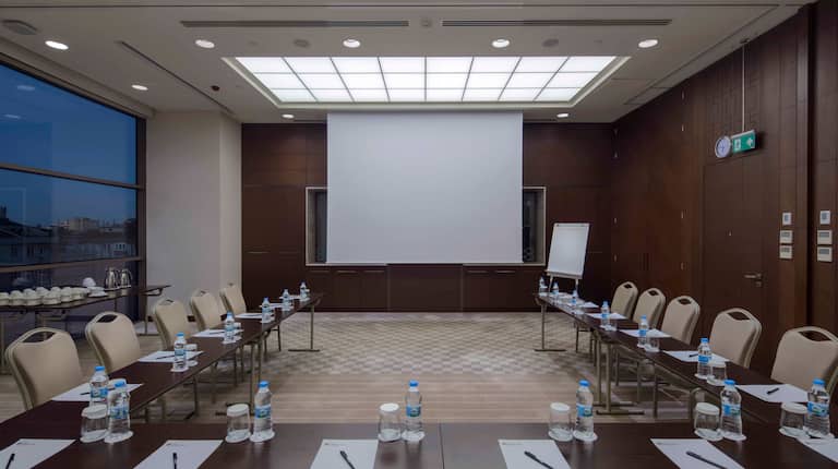 View of Camlica Meeting Room From Rear with Large Table in U-Shape Setup, Projector Screen and Outside View