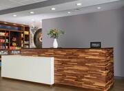 The front desk at a Hampton by Hilton. The desk is made of various colored wood with a warm gray backdrop. 
