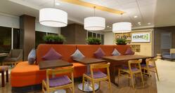  Oasis Lobby Lounge With Decorative Lighting, Wood Chairs and Table Seating by Large Orange Sofa, and TV in Background