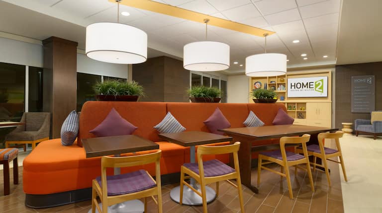  Oasis Lobby Lounge With Decorative Lighting, Wood Chairs and Table Seating by Large Orange Sofa, and TV in Background