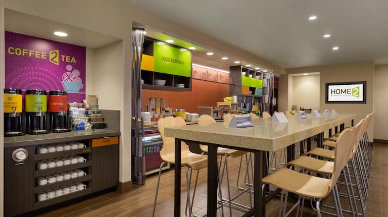 Brightly Lit Hot Beverage Service Area by Community Table With View of Food Service Area and TV in the Background