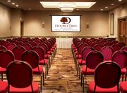  Meeting Room Arranged Theater Style With Rows of Red Chairs Facing Speaker's Table With White Linens and Presentation Screen