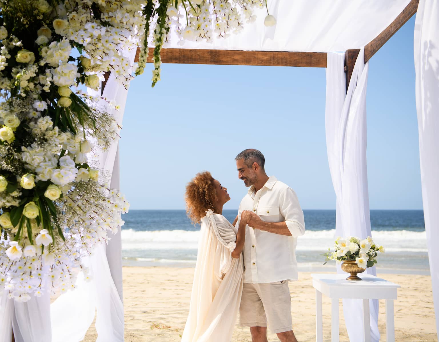 A couple getting married under a wooden trellis on the beach.